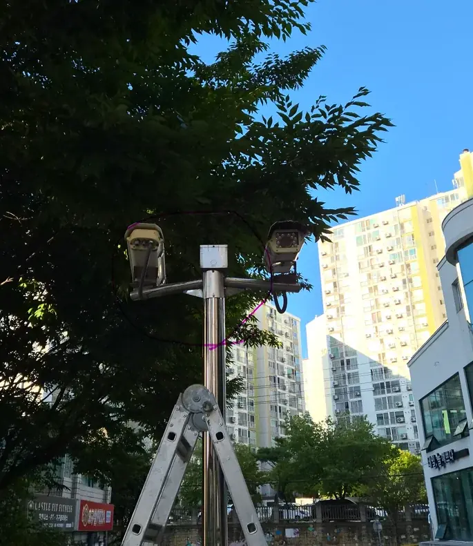 오산 공장 출입구 CCTV 기둥 파손 수리 현장, 사다리 앞에 선 스테인리스 기둥과 감시카메라